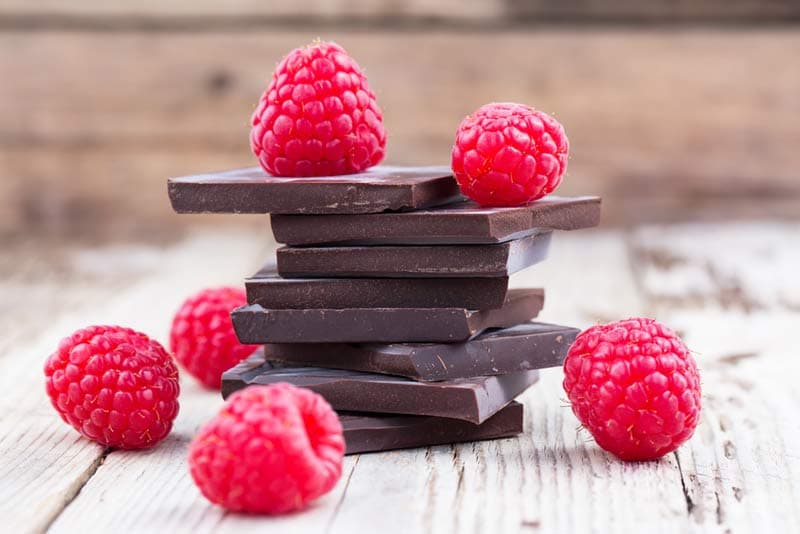 Pieces of dark chocolate with raspberries around it