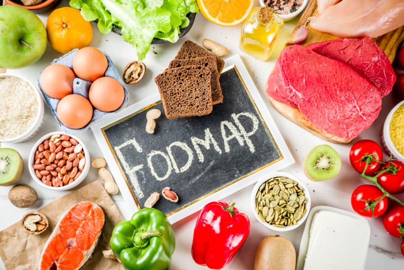 A whiteboard with the word 'FODMAP' on it. Various fruits and vegetables surround it.