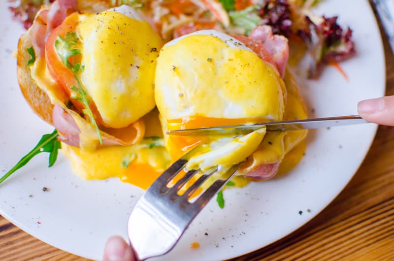 Poached eggs on a plate being eaten with a fork and knife