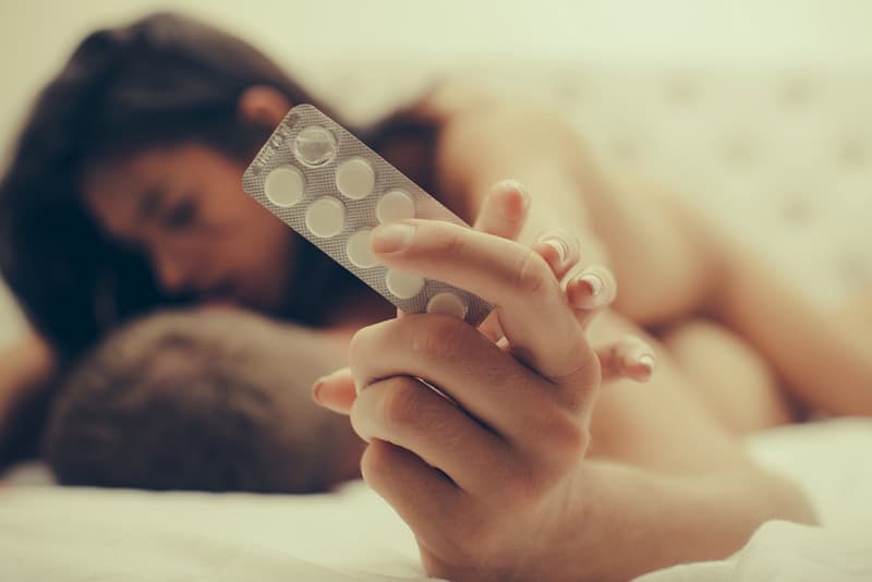 A man holding a blister pack of medication in his hands whilst engaging in sexual activities with a lady