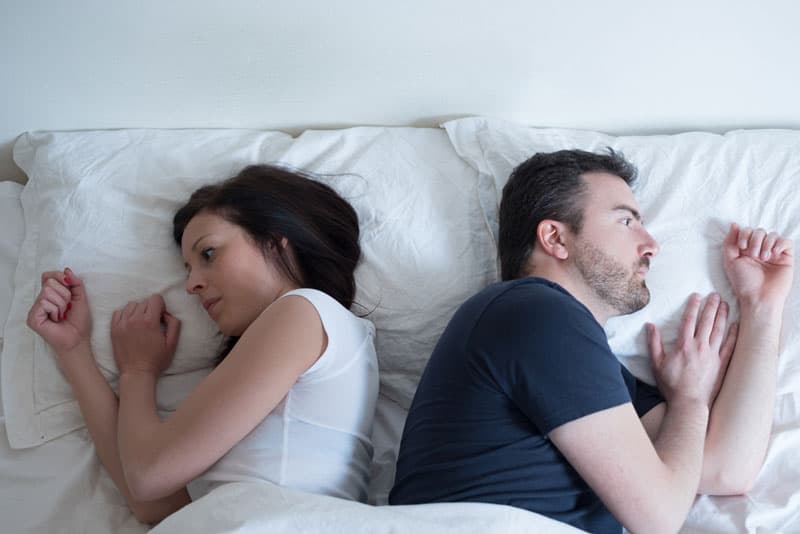 A man and woman sleeping away from each other looking dissatisfied