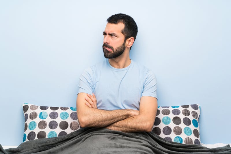 A man looking unsatisfied whilst sat in bed