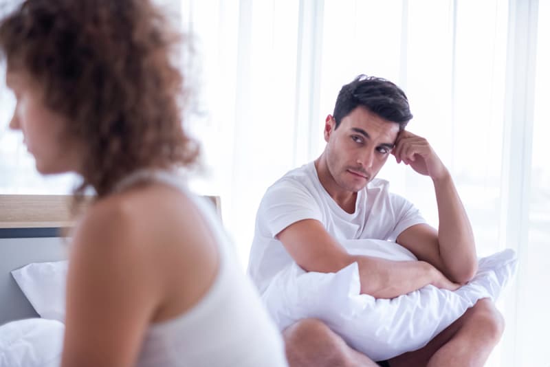 A man looking frustrated whilst staring at his female partner as he sits on his bed