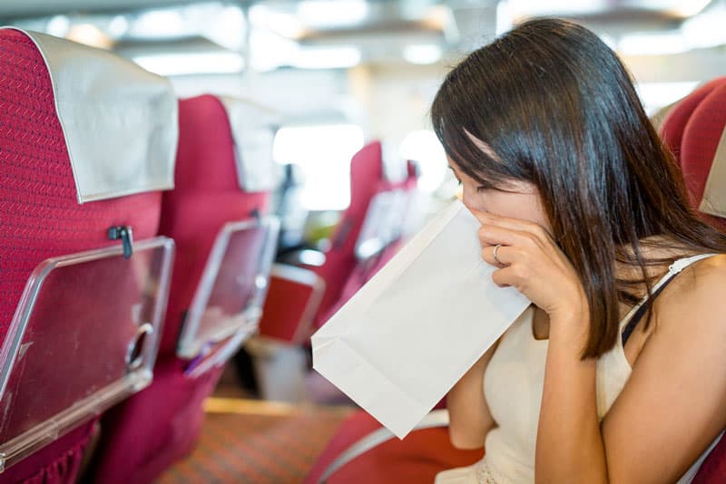 A lady being sick into a bag on a moving plane