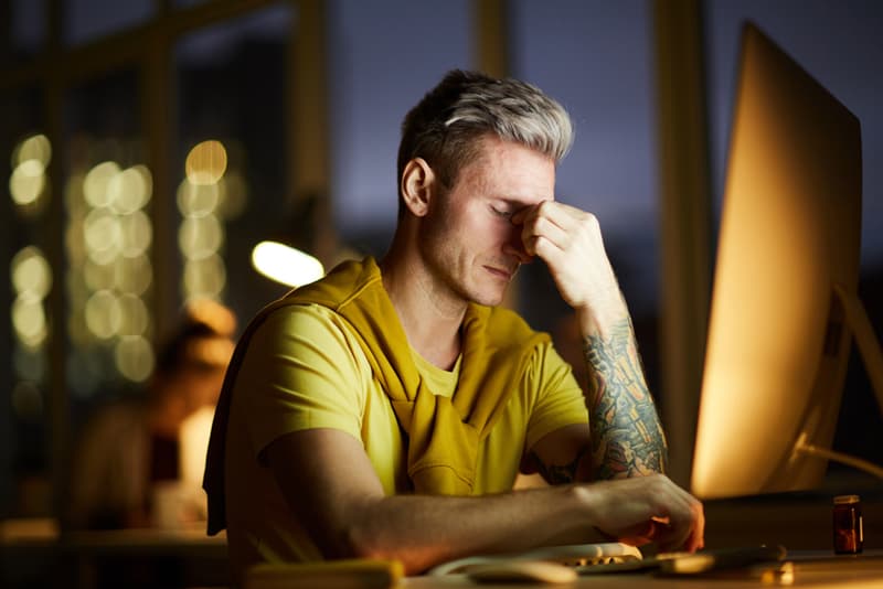 A man sat at an office desk whilst suffering from a migraine headache