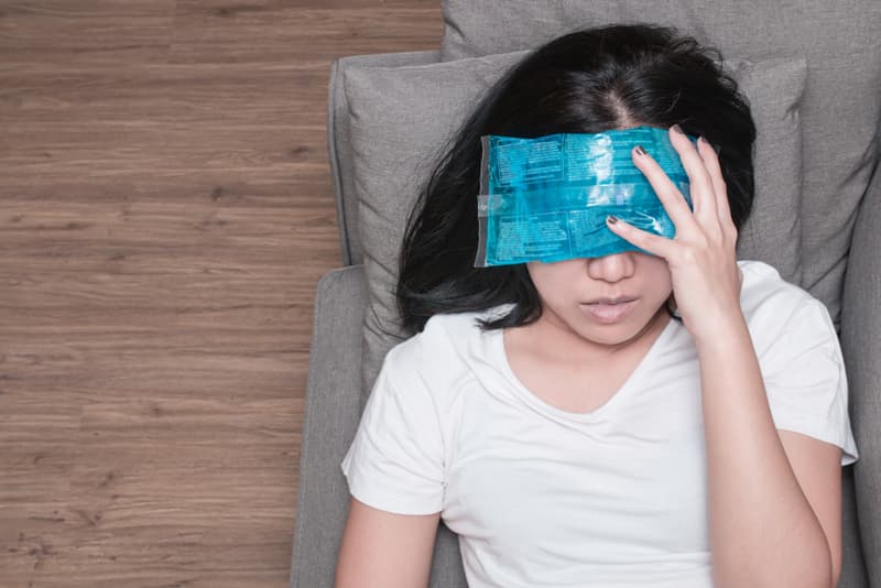 A lady applying a cold pack to her head to soothe her migraine