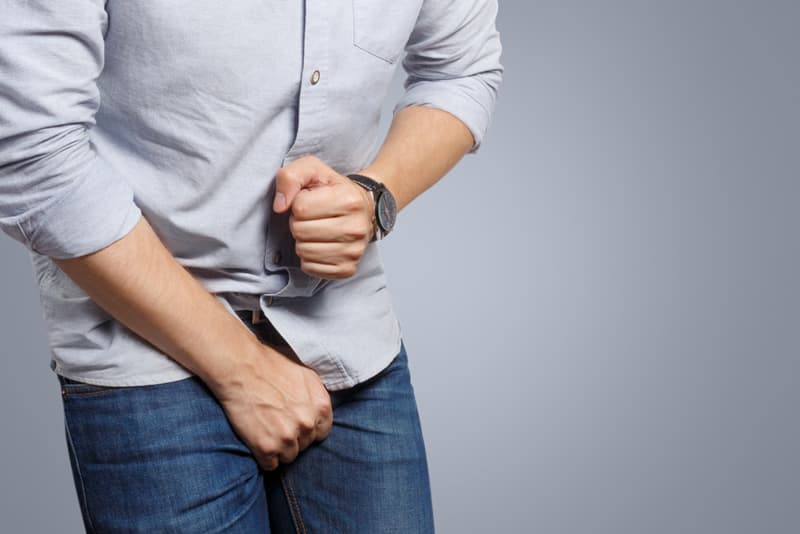 A man crouching in discomfort with his hand on his crotch