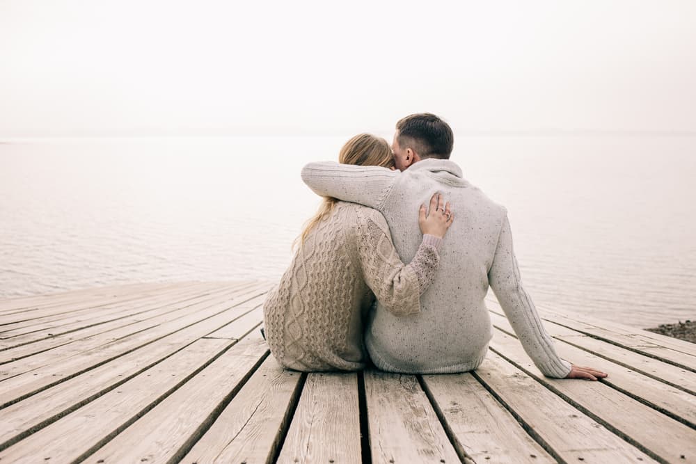 A man and a lady sat together in front of a sea view hugging each other