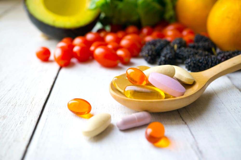 Fertility supplements on a spoon in front of some fruits and vegetables