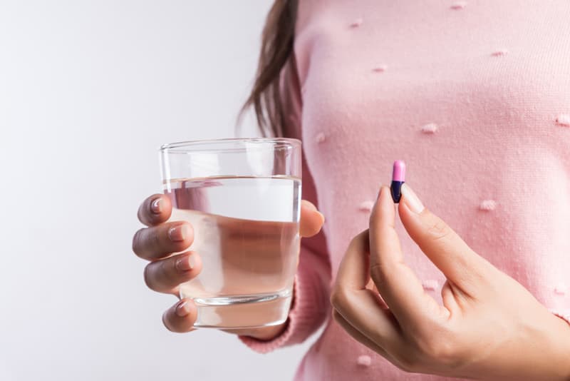 A lady holding a metronidazole tablet and a glass of water