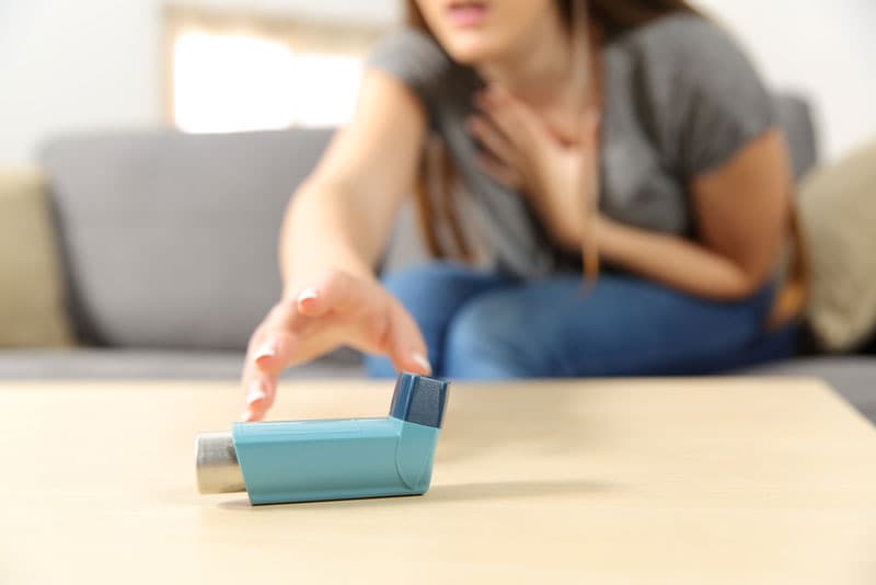 A lady suffering from an asthma attack, reaching out for a ventolin inhaler on the table in front of her