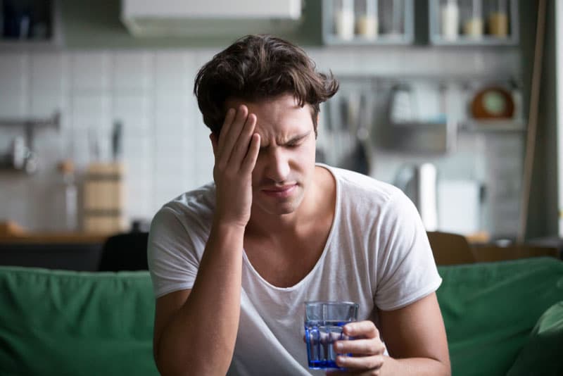 A man struggling to cope with a migraine whilst holding a glass of water