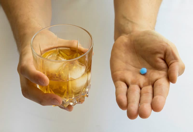 A pair of hands holding a glass of alcohol and a Viagra pill