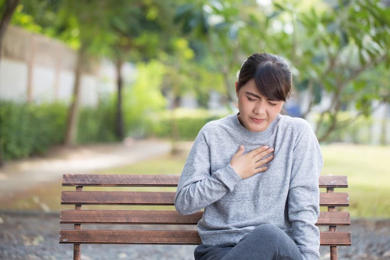 A lady looking uncomfortable whilst sat at a bench in the park