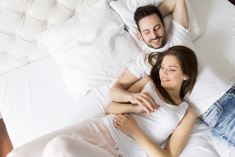 A man and lady lying together on a bed looking happy