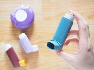 A hand holding up an inhaler with other inhalers laying on the surface below