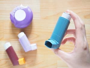 A hand holding up an inhaler with other inhalers laying on the surface below