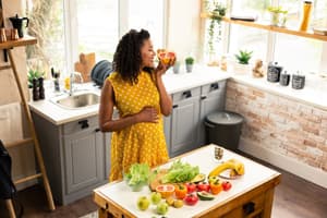 A lady stood in a kitchen with vegetables spread out on a table in front of her