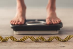 A person stood on some weighing scales with a tape measure on the floor in front of the scales