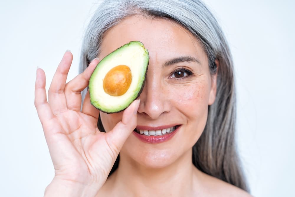 Woman holding an avocado in front of her face