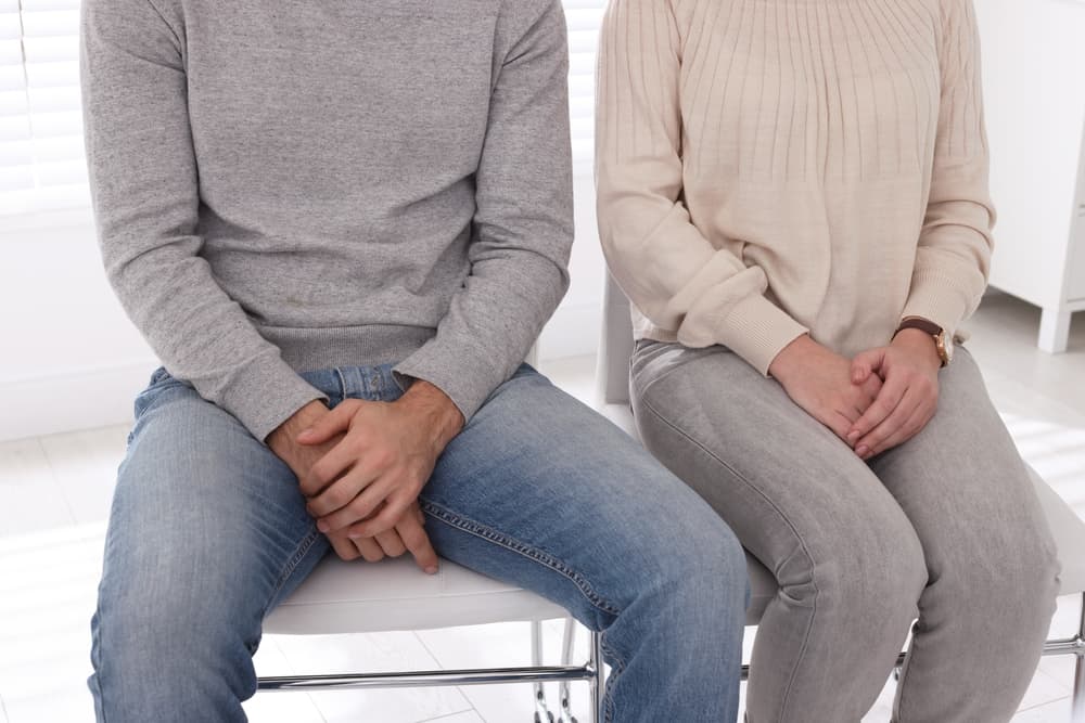 Man and woman sat next to each other covering their genital areas with their hands, indicating they are suffering from genital herpes