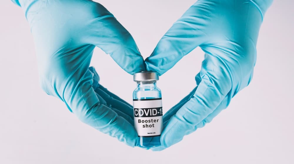 COVID booster vaccine being held by hands with rubber gloves on them