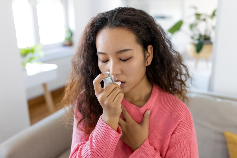 A lady taking a pump of the blue asthma inhaler, Ventolin (salbutamol)