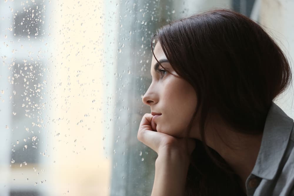 Lady looking outside from a glass that has rain on it