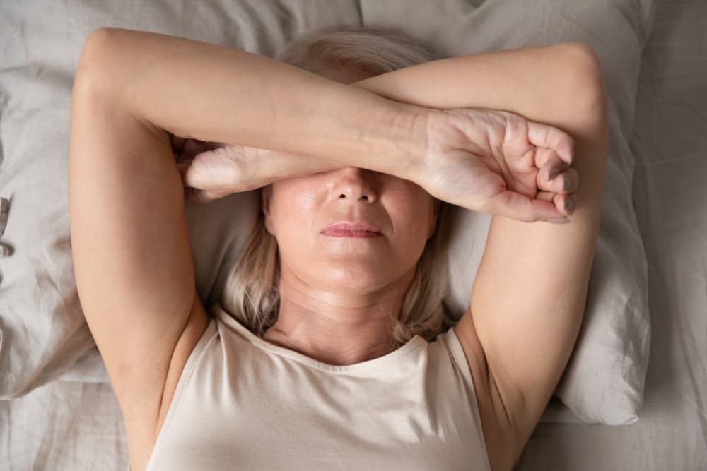 Woman lying on her bed covering her head because she is experiencing menopause symptoms