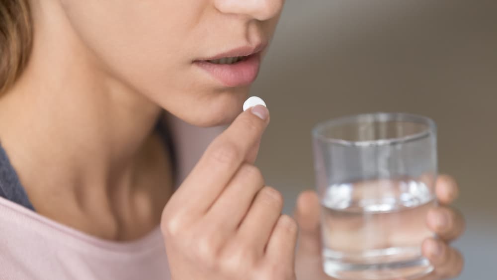 Woman with paracetamol in one hand and a glass of water in the other hand