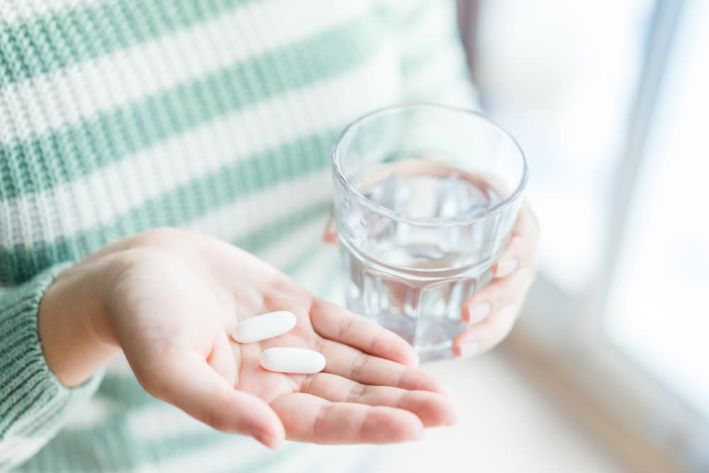 Paracetamol being held in one hand with a glass of water in the other hand