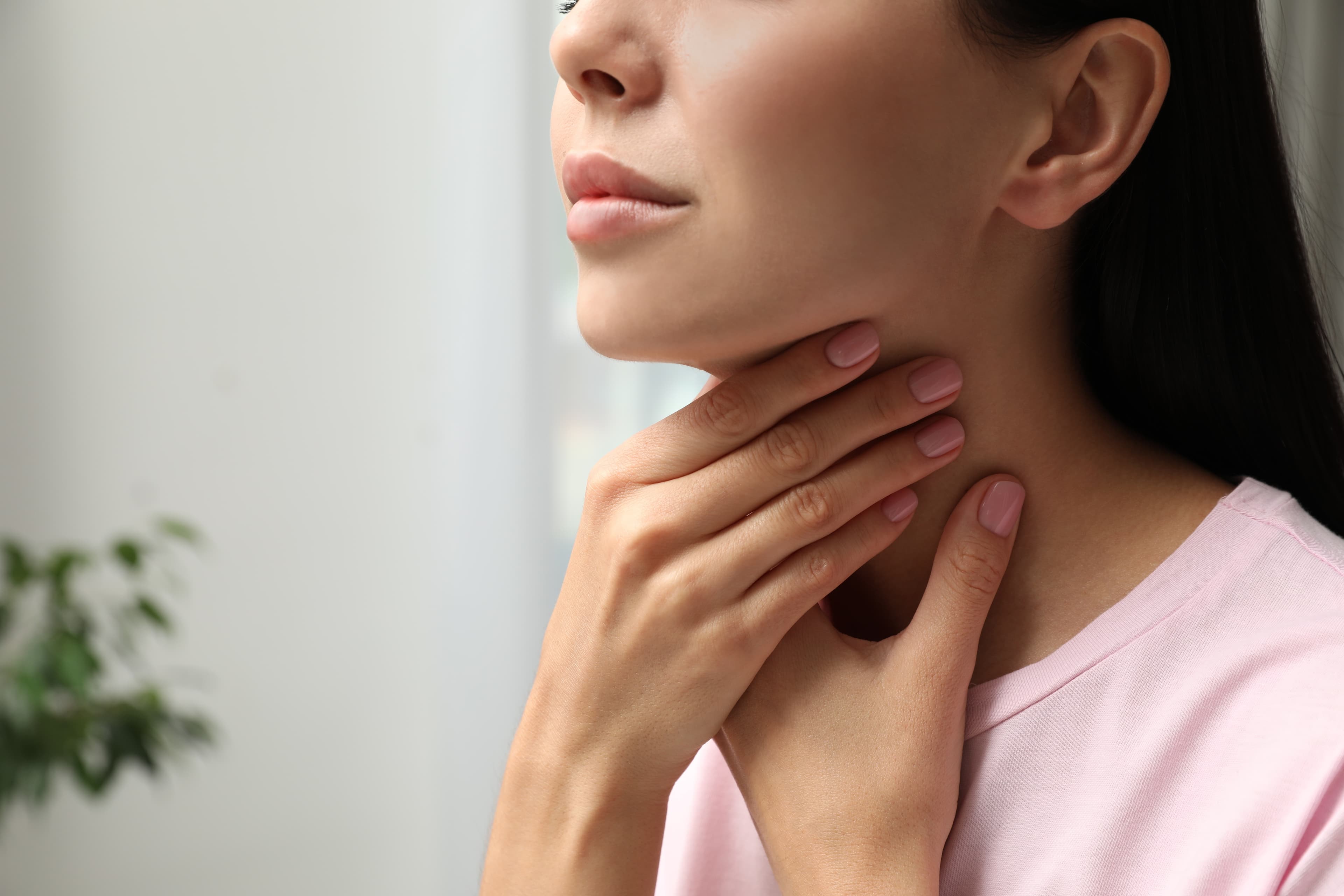 A lady feeling her throat whilst experiencing a problem with her thyroid gland