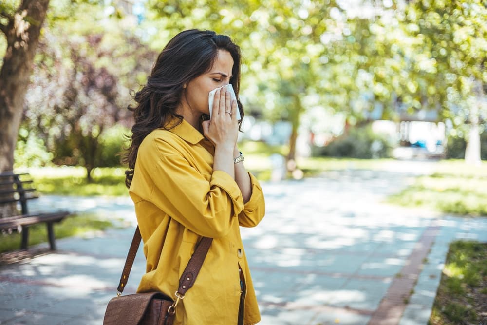 A lady suffering from hay fever whilst walking in a park in Europe